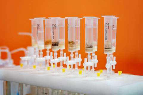 Fiolki z substancjami chemicznymi PFAS do badań w laboratorium, pomarańczowe tło.